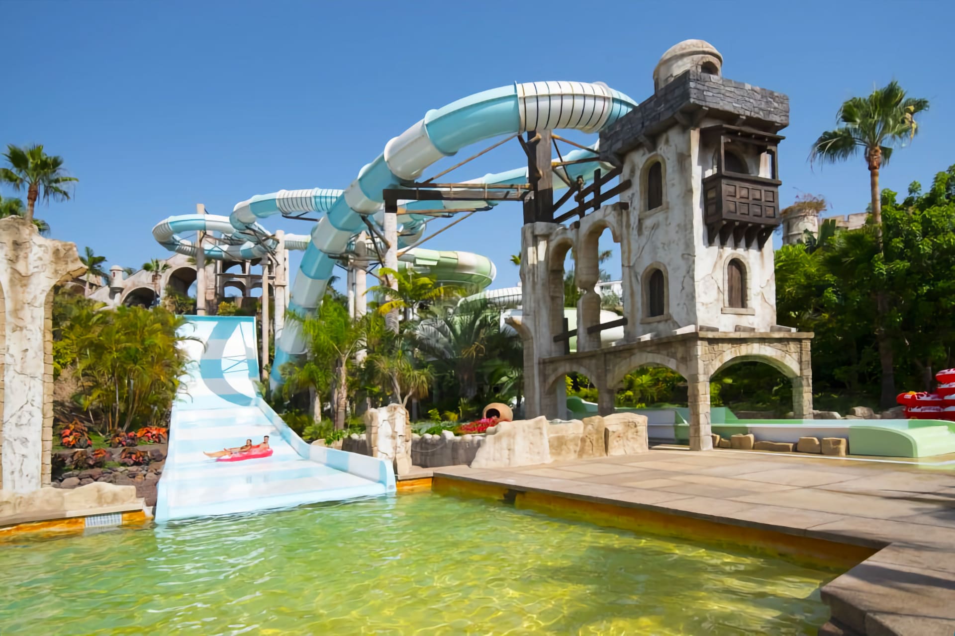 Excited families enjoying the wave pool at Aqualand Costa Adeje, with towering water slides in the background